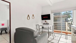 Un soggiorno moderno con un divano grigio, un tavolo da pranzo piccolo con sedie, una TV a parete e un balcone con vista sull'esterno.