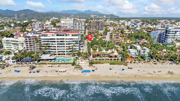 Una veduta costiera con un hotel sulla spiaggia, caratterizzato da numerosi piani, una piscina e ombrelloni.