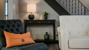 A living room with a dark blue armchair, a white armchair, and a lamp on a console table. - Champion Center Accommodations - 6 beds, 2 bath (Appleton)