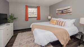A bedroom with a bed, a television, a window with curtains, a painting, and a bedside table. - Champion Center Accommodations - 6 beds, 2 bath (Appleton)