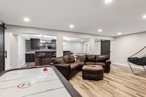 A modern living room with a pool table, leather sectional sofa, and a dining area.