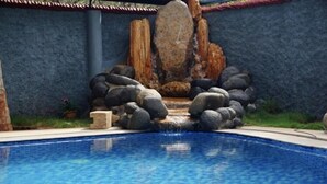 Una piscina con caída de agua rodeada de rocas y un muro de piedra.