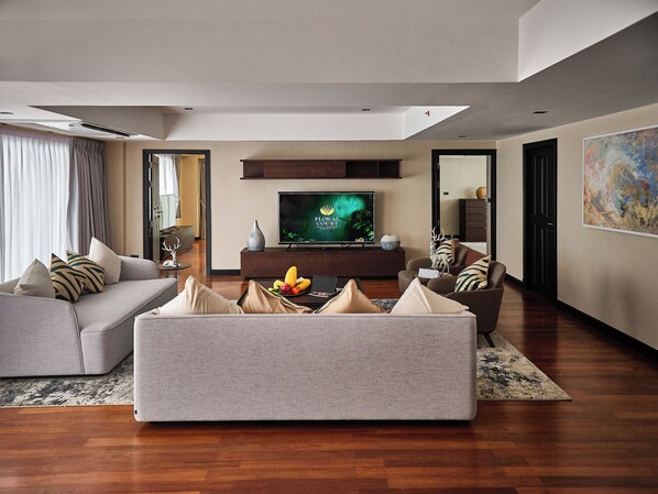 A modern living room with a grey sofa, a coffee table with fruit, and a flat-screen TV on a wooden stand. - Floral Court Hotel & Residence Sukhumvit 13 (Bangkok)