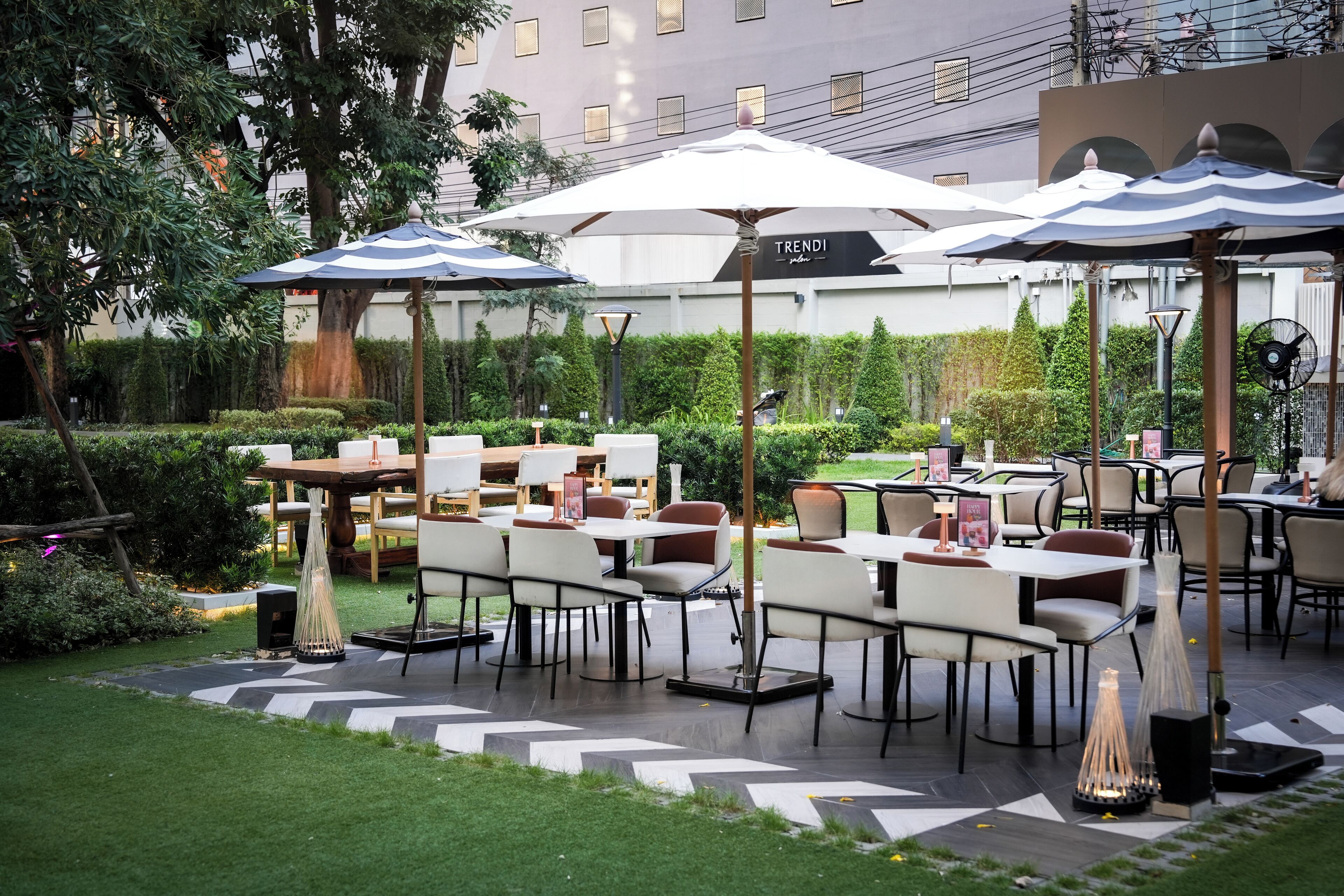 An outdoor dining area with tables and chairs, umbrellas, and a sign that reads "TRENDI."