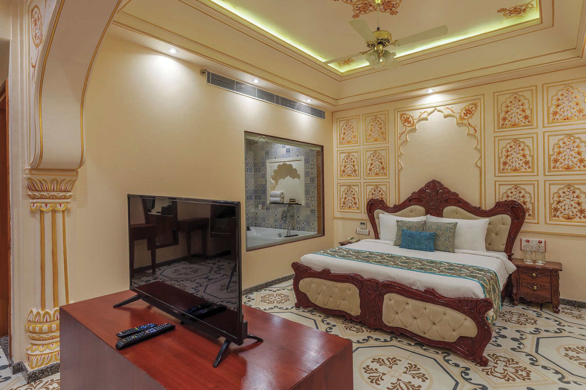 A bedroom with a large bed, a TV, and a desk with remote controls.