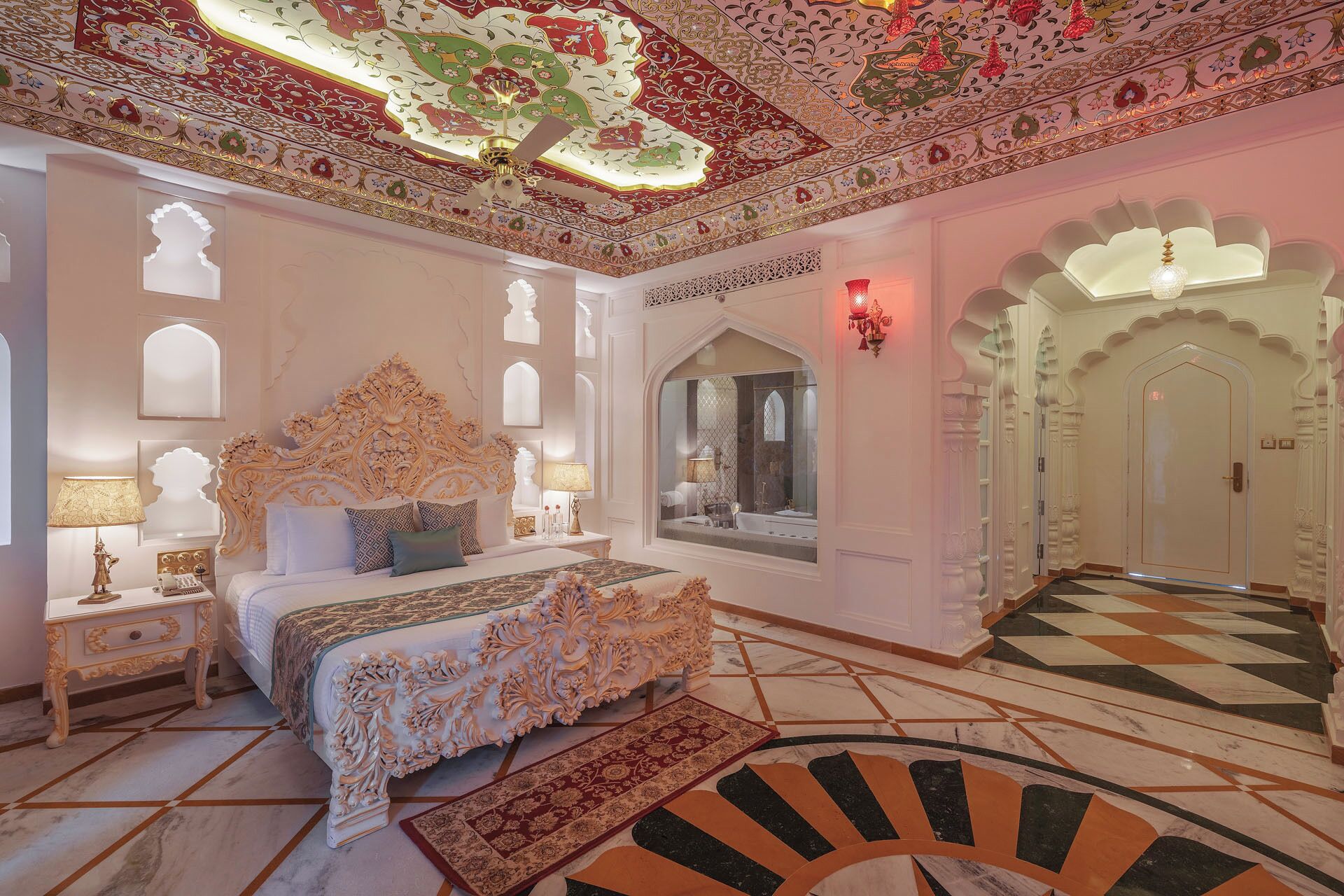 A luxurious bedroom with an ornate ceiling, a large bed, and a view of a bathroom through a window.