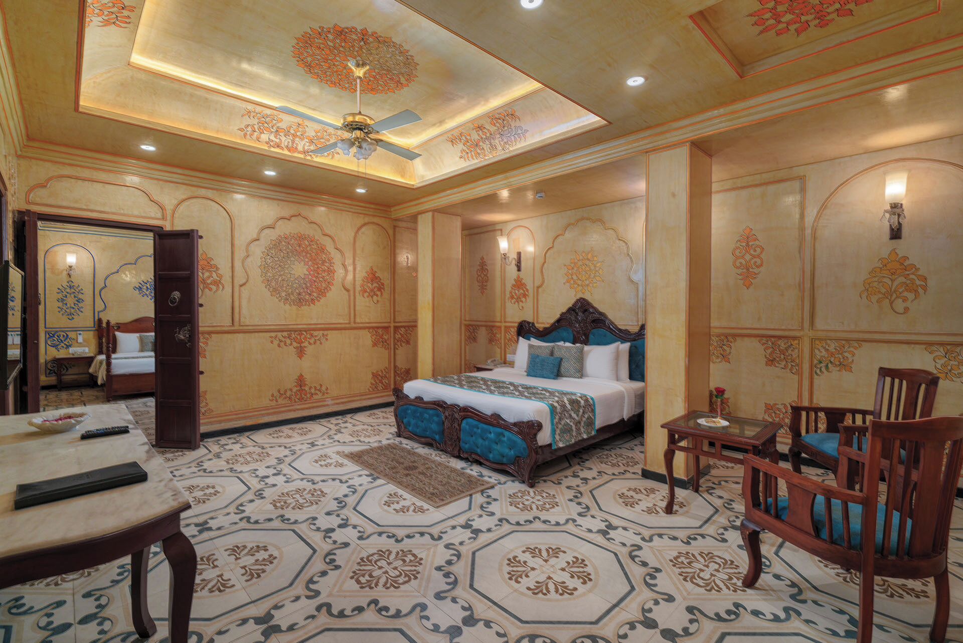 A bedroom with a large bed, a ceiling fan, a small table, and a chair.