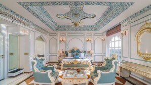 A luxurious room with ornate ceiling, a large bed, and a seating area with chairs and a table. - R Chandras Palace  (Chomu)