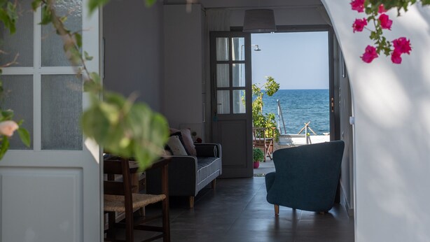 Vista interna de um quarto com vista para o mar, um sofá, uma poltrona e uma mesa de jantar.