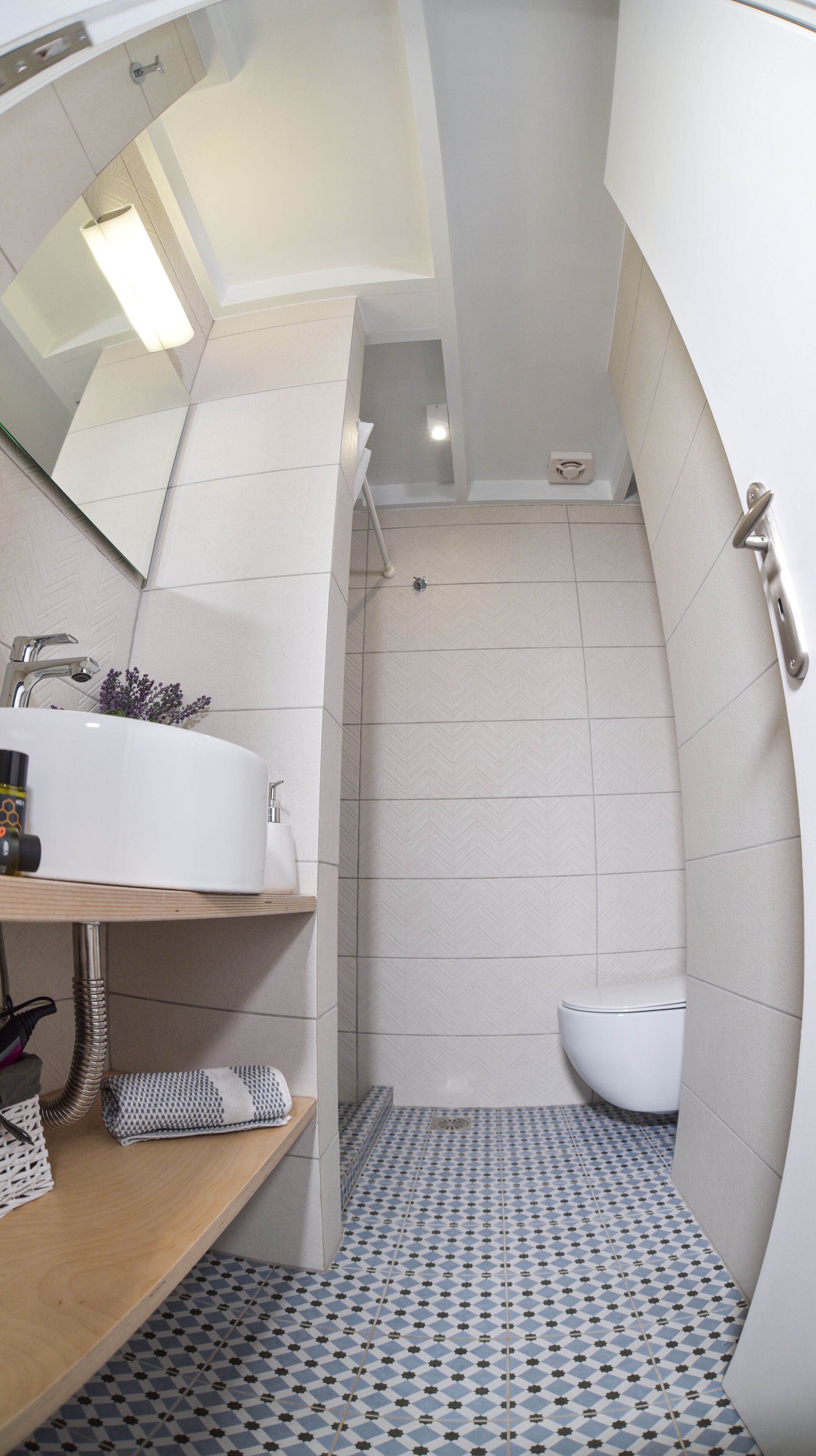 Een moderne badkamer met een wit wastafelmeubel, spiegel en toilet. De vloer heeft een geometrisch tegelpatroon.