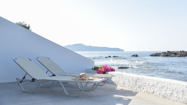 Zwei Liegestühle mit Hut und Blumen auf einem Balkon mit Blick auf das Meer.