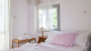 Ein Schlafzimmer mit Holzboden, einem Bett mit rosa-weißer Bettwäsche, einem Nachttisch mit Lampe und einem Fenster mit Vorhängen.