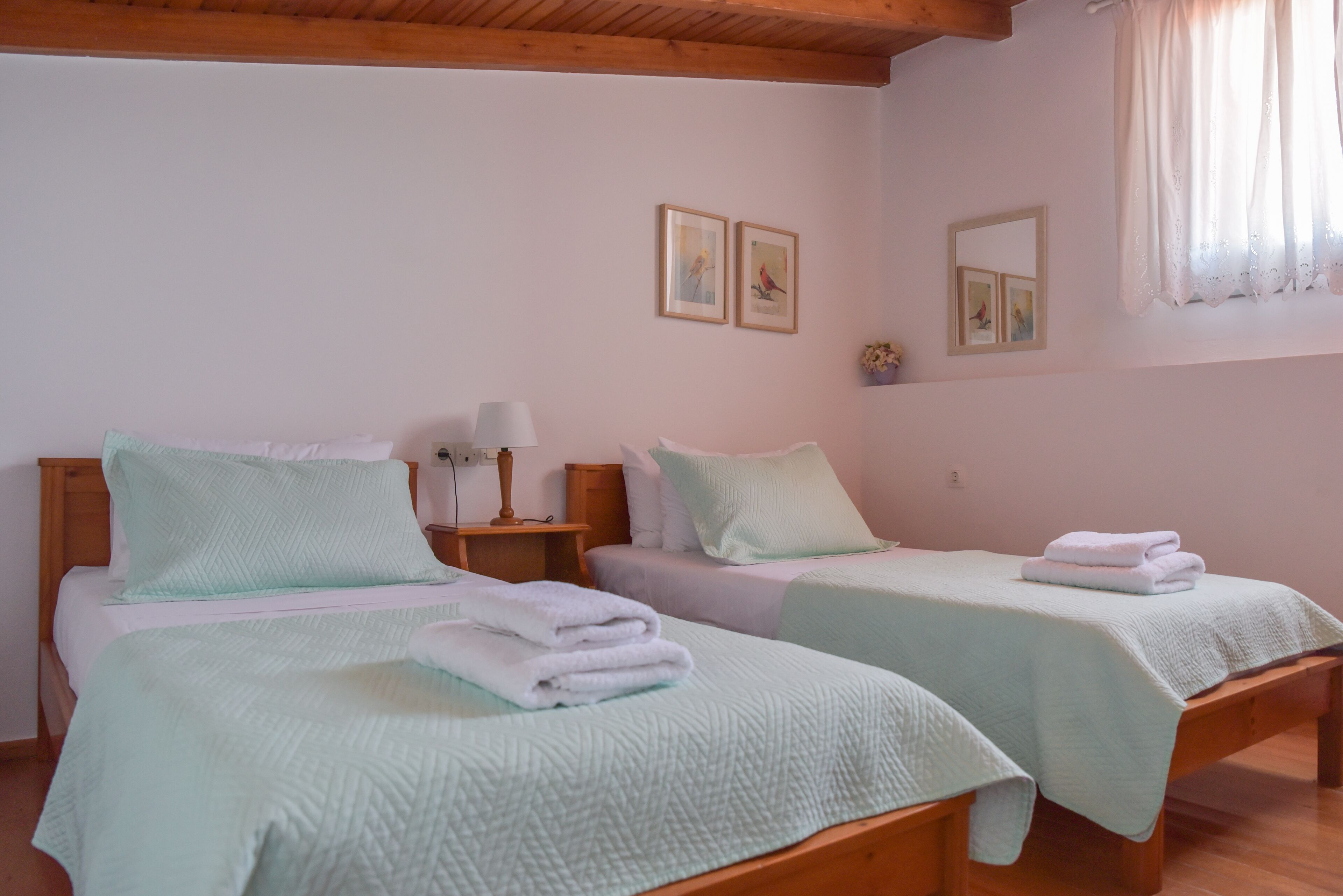 Dos camas individuales con ropa de cama verde claro, cabeceros de madera y mesitas de noche con lámparas.