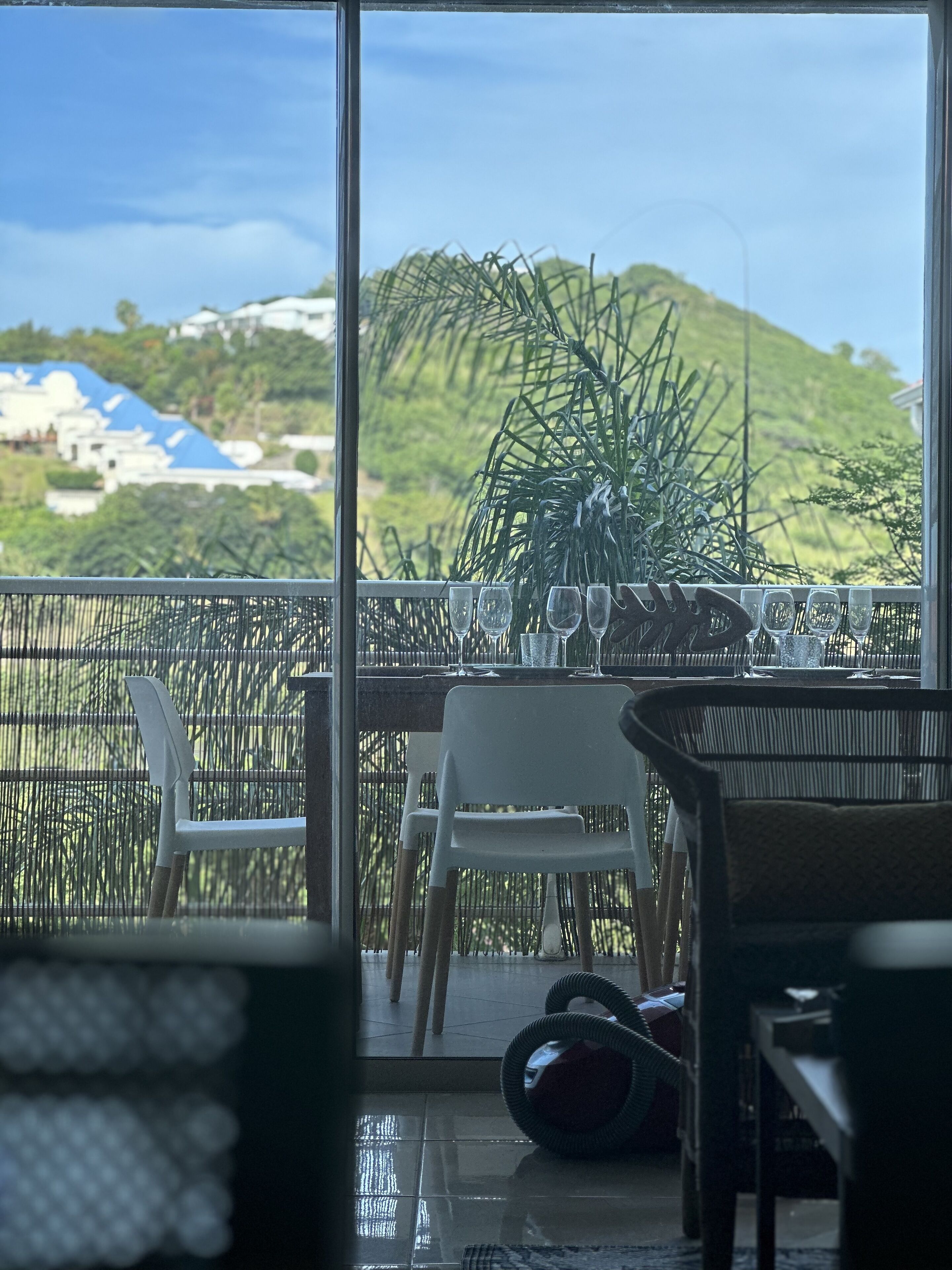 Un balcón con mesa lista para comer, sillas y vista a un paisaje verde.