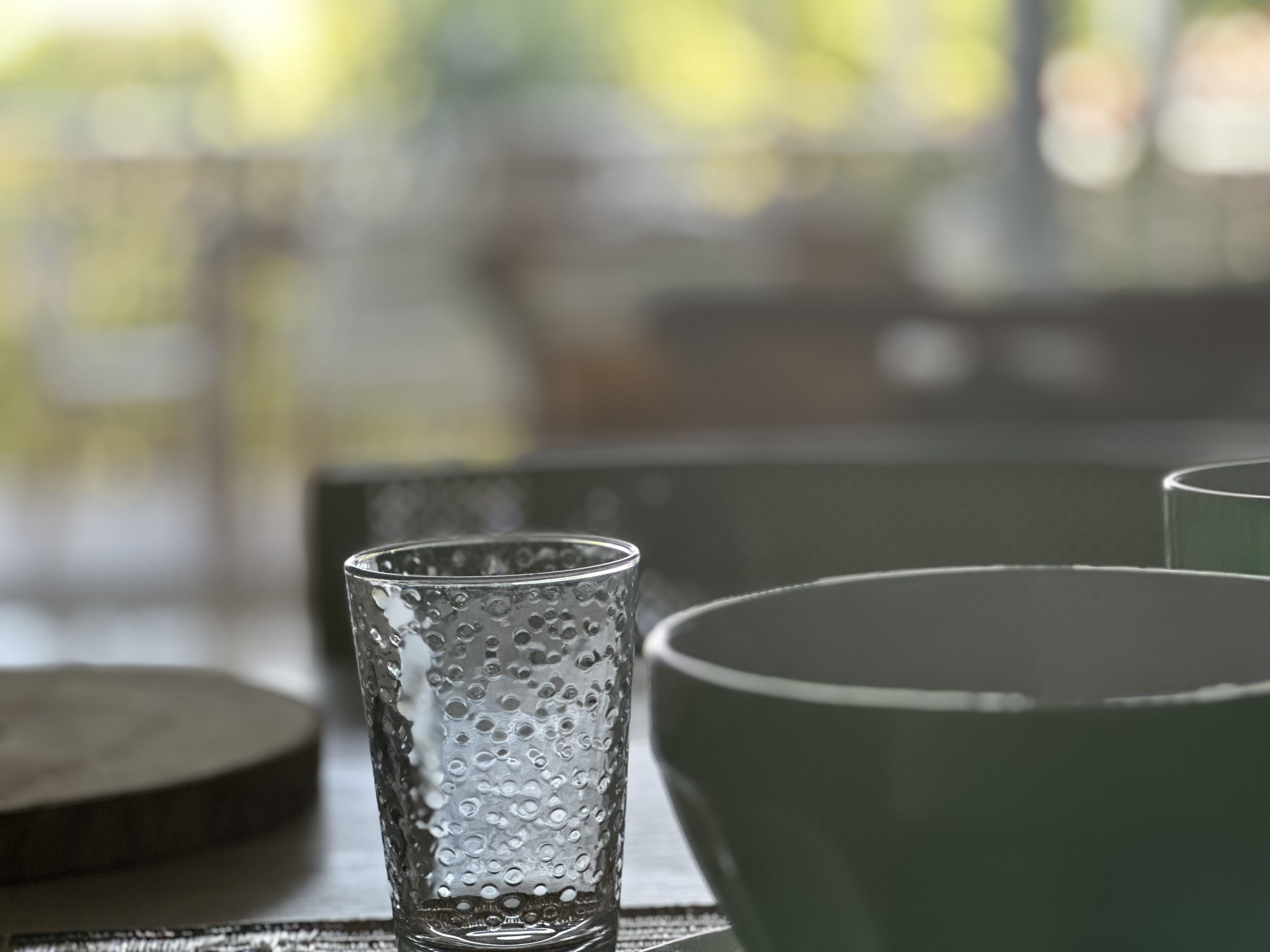 Et glas med et struktureret mønster og en grøn skål på et bord.