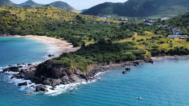 A coastal area with a beach, rocky shoreline, and a small boat in the water. - Cosy  Apt on friar’s bay SxM . 2 min to the Friar’s Bay beach ,restaurants (Saint Martin)