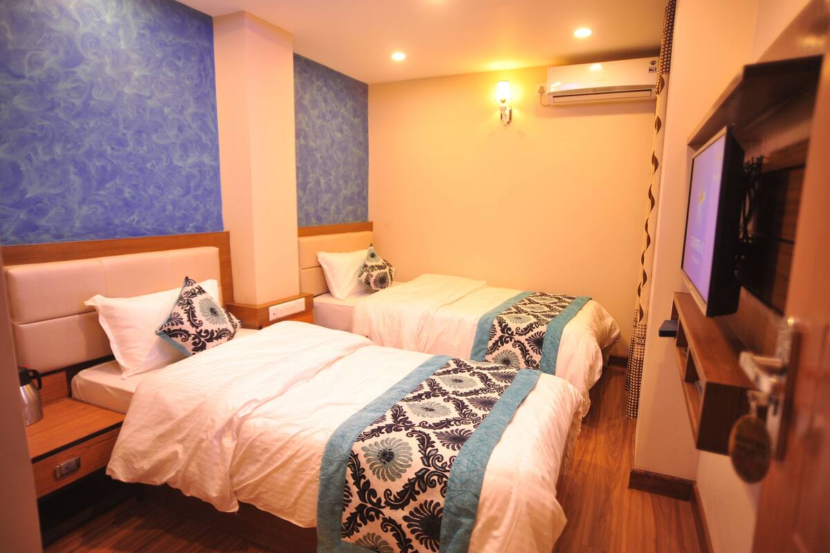 A hotel room with two beds, a TV, an air conditioning unit, and a wooden floor.