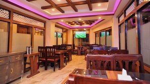 A restaurant with wooden furniture, a TV screen, and a ceiling with wooden beams and purple lighting. - Hotel Aarati (Kathmandu)
