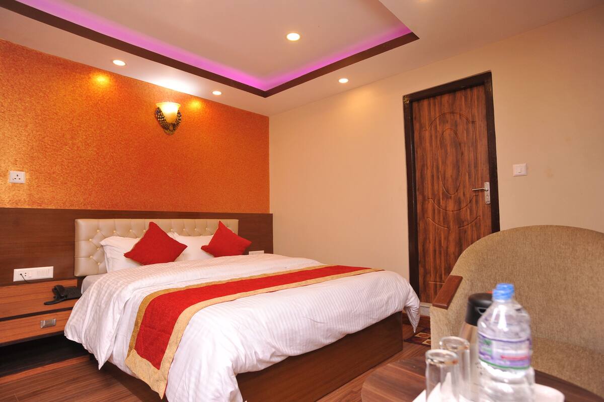 A hotel room with a large bed, a wooden headboard, a nightstand, a chair, and a water bottle on the table.