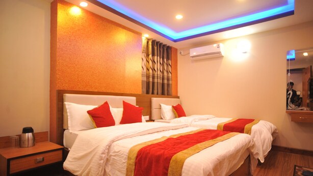 A hotel room with a large bed, a nightstand, and a wall-mounted air conditioner. - Hotel Aarati (Kathmandu)