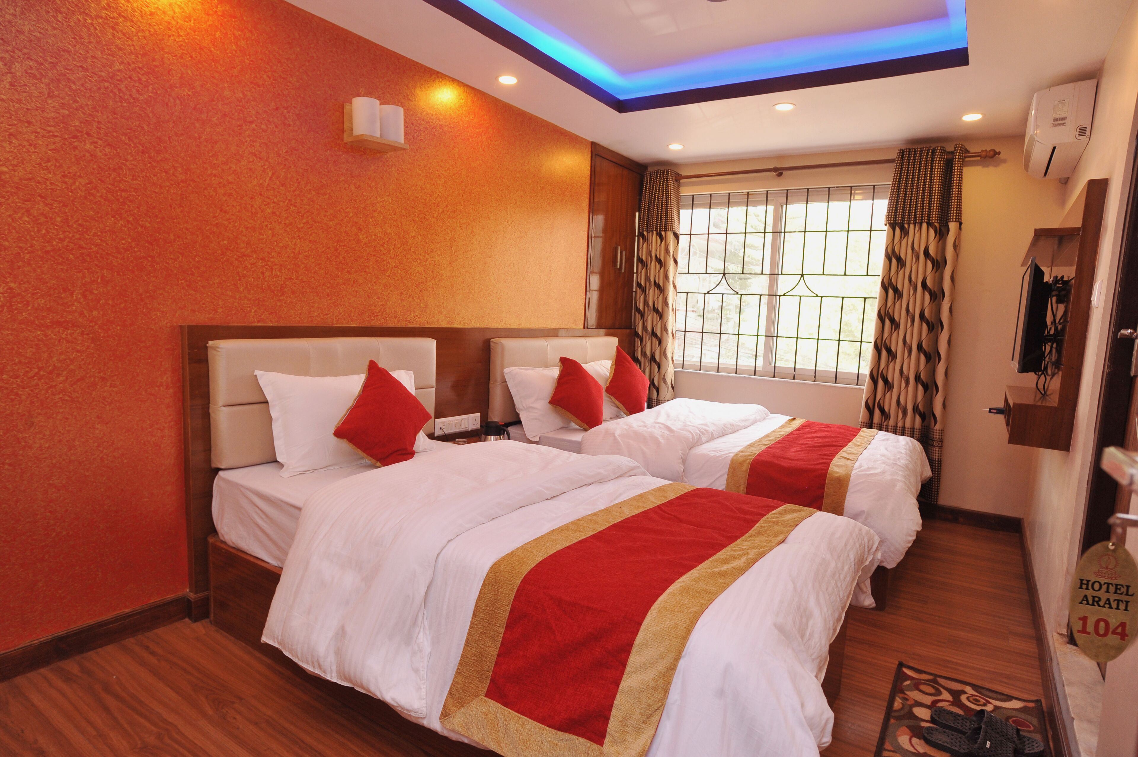 A hotel room with two beds, red and white bedding, a wooden floor, and a window with patterned curtains.