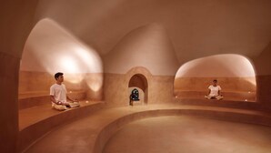 Ein Meditationsraum mit zwei Personen, die auf Bänken sitzen, einem zentralen Altar und einem gewölbten Deckenbau.