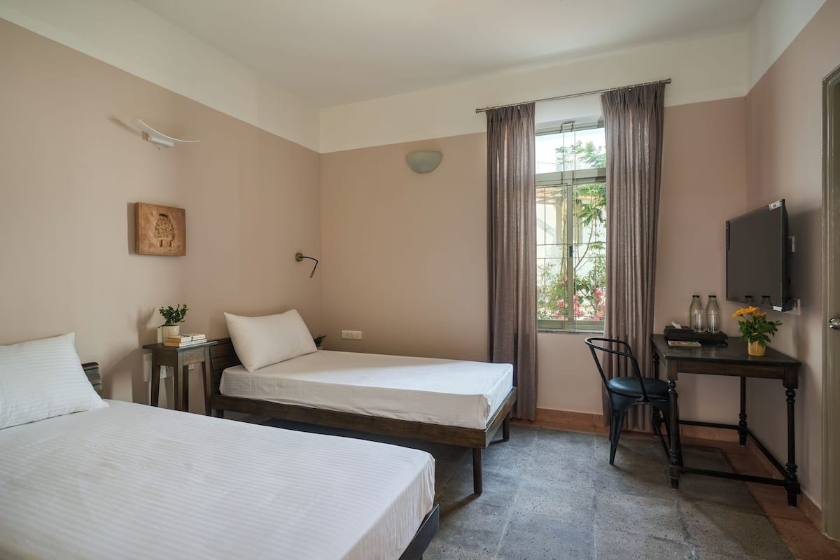 Ein Hotelzimmer mit zwei Betten, einem Schreibtisch mit Stuhl, einem Fernseher und einem Fenster mit Vorhängen.