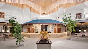 Eine großzügige Lobby mit einer zentralen Statue, einem Empfangsbereich und einer hohen Decke mit Holzleisten.