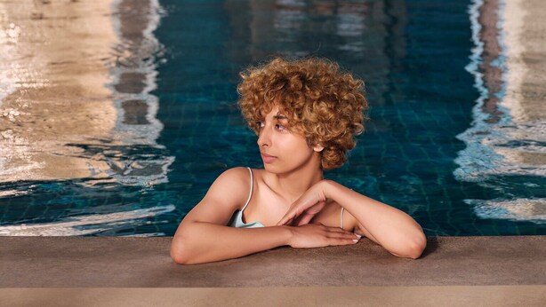 Eine Person in einem Schwimmbecken, im Hintergrund eine Wand mit Verzierungen und eine Uhr.