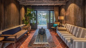 Um quarto aconchegante com teto de madeira, um sofá, um banco, uma mesa e um vaso com planta.