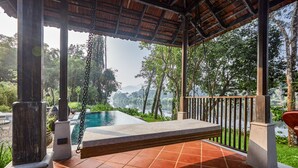 Área de estar coberta ao ar livre, com vista para uma piscina e um lago.