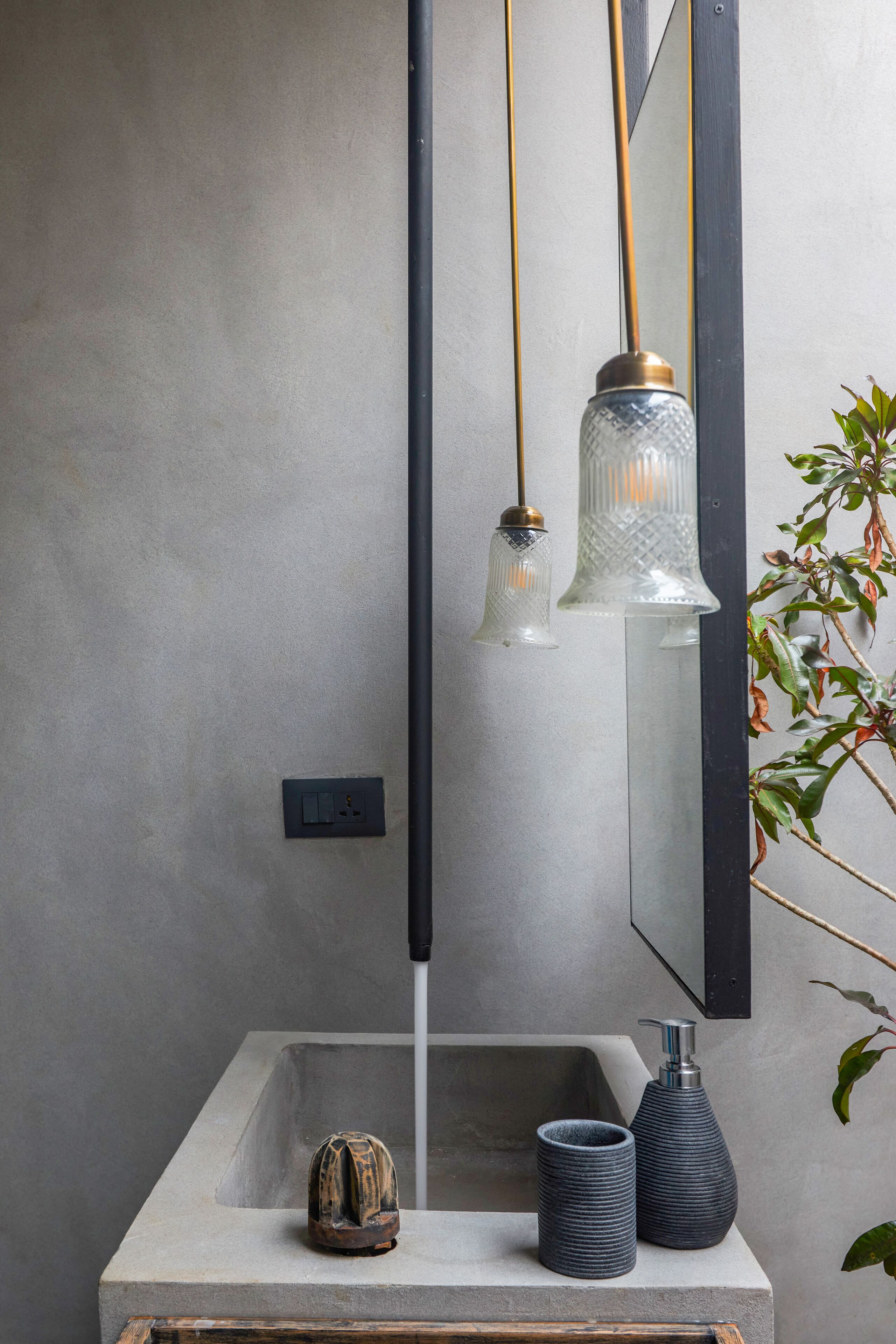 A bathroom with a concrete sink, two dark vases, a wooden object, and a mirror with a black frame.