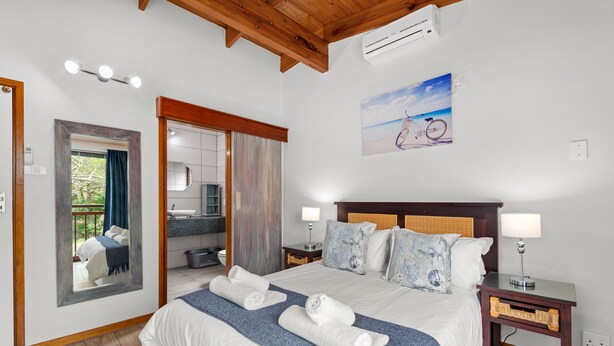 A hotel room with a large bed, two bedside tables, a mirror, and a painting of a bicycle on the wall. - San Lameer Villa 2704 (Southbroom)