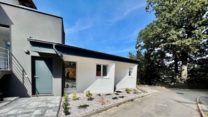 Una casa moderna de dos pisos con fachada gris, una puerta principal y un pequeño jardín con grava y plantas.