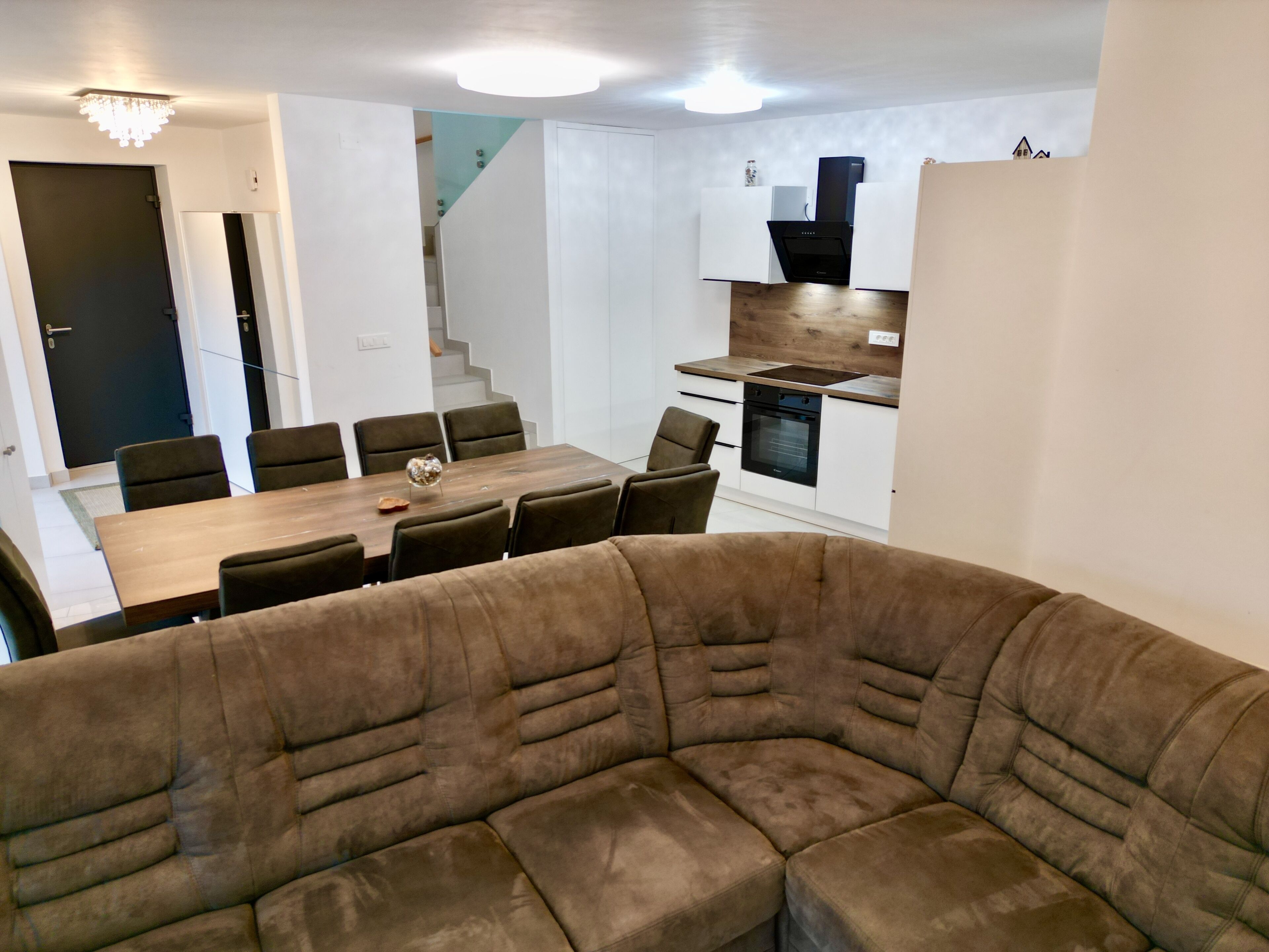En moderne stue med en stor hjørnesofa, et spisebord med stole, og et køkken med komfur og ovn.