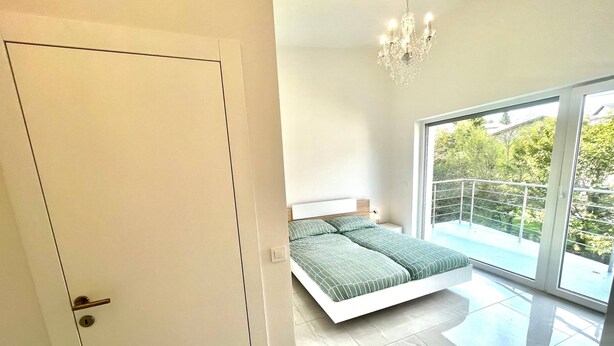 Un dormitorio con cama, candelabro y balcón con vistas a zonas verdes.