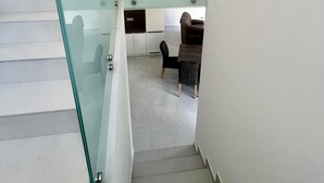 Una escalera moderna con barandales de vidrio que conduce a un comedor con mesa y sillas.