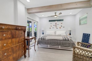 A bedroom with a wooden dresser, a bed with a patterned bedspread, a ceiling fan, and a wall with decorative fish art.