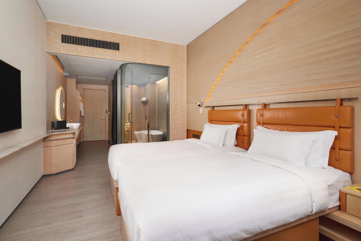 Ein Hotelzimmer mit einem großen Bett, einem Nachttisch, einem Spiegel und einem an der Wand befestigten Fernseher.