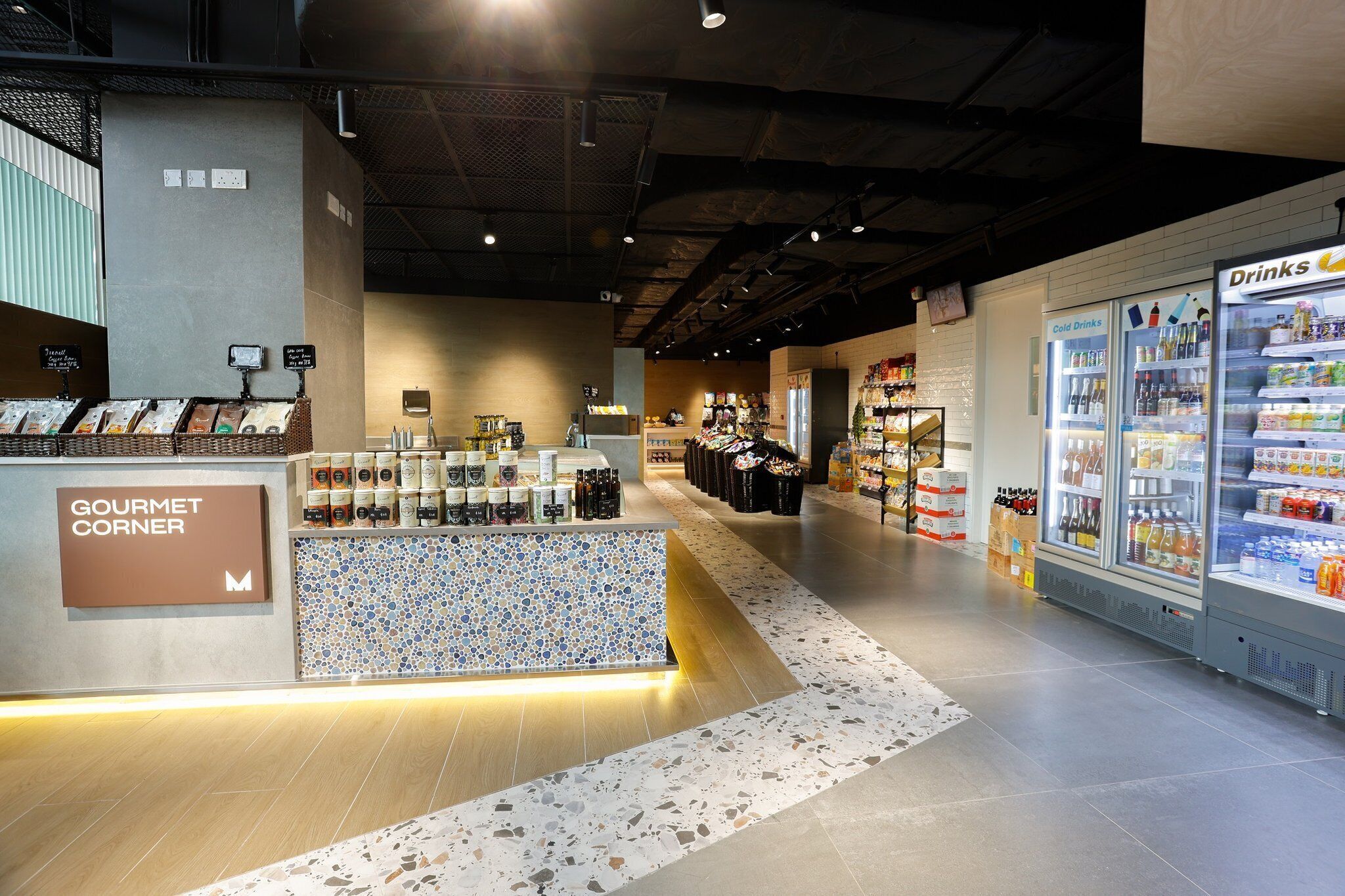 A grocery store interior with a 'Gourmet Corner' section, refrigerated drink cases, and a variety of packaged goods.