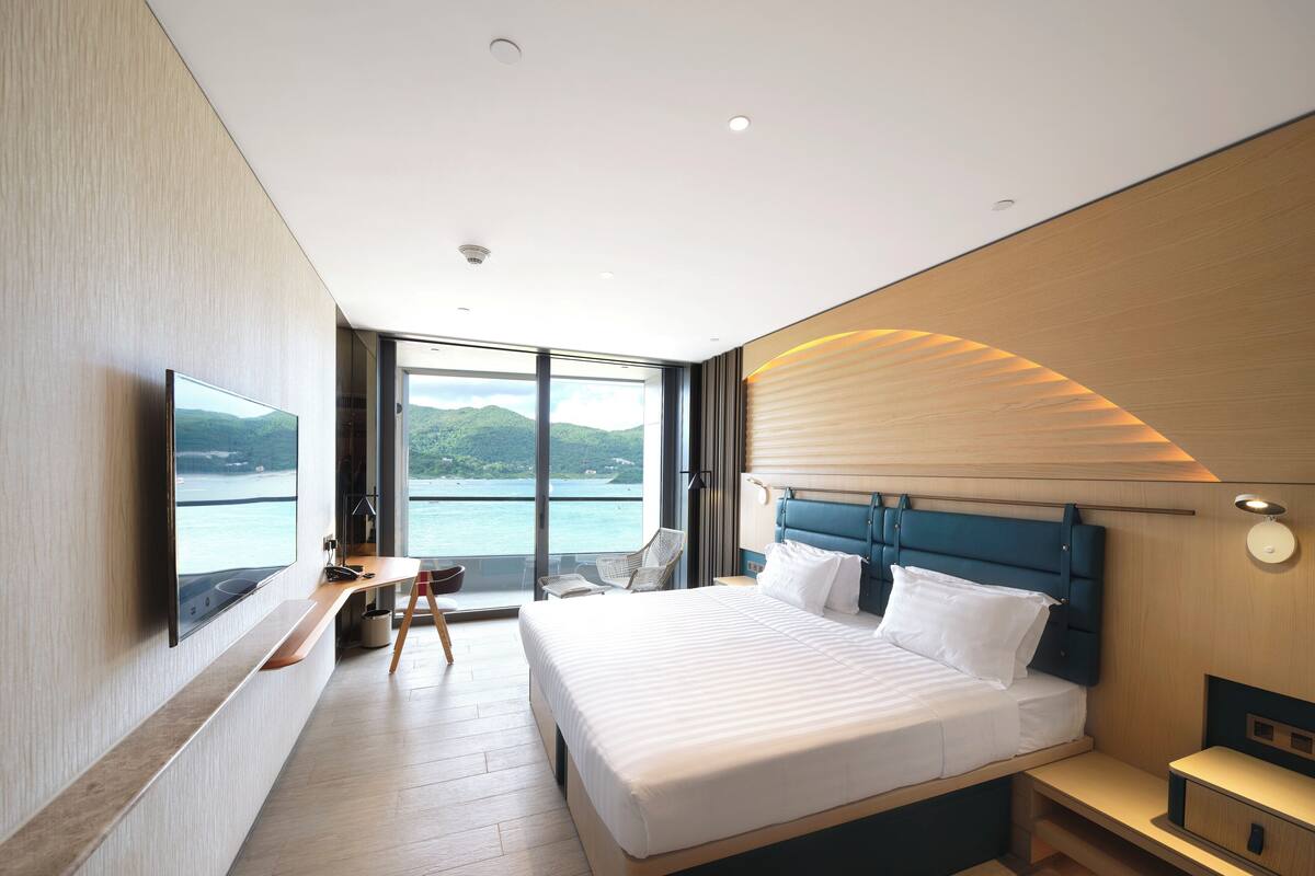 A modern hotel room with a large bed, a desk, a chair, and a TV.