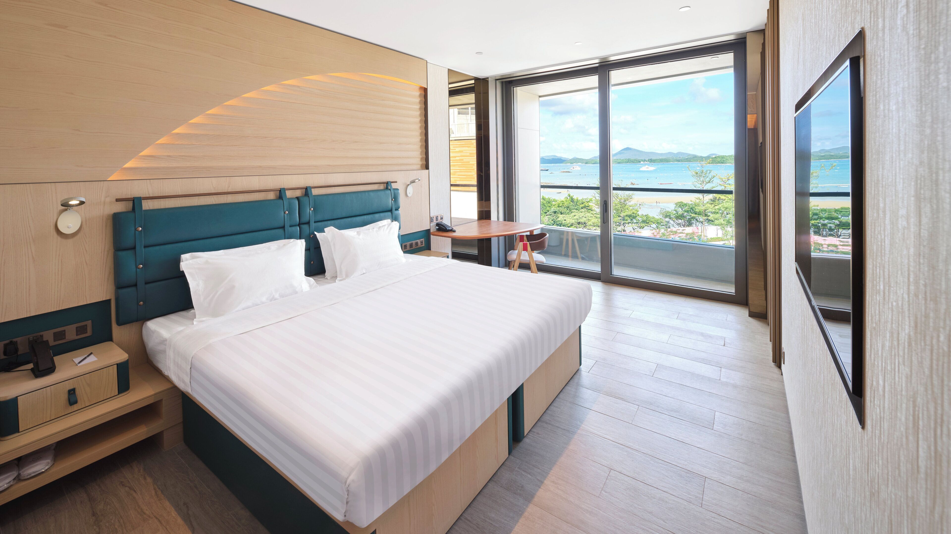 Habitació d'hotel moderna amb un llit gran, una taula de treball, una cadira i un balcó amb vista al mar.