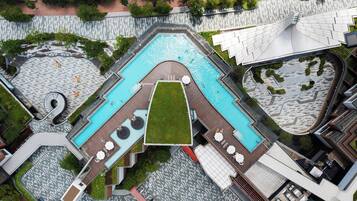 An aerial view of a modern hotel with a central swimming pool, multiple lounge areas, and a landscaped garden.