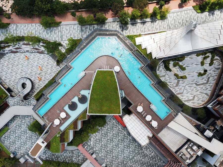 An aerial view of a modern hotel with a central swimming pool, multiple lounge areas, and a landscaped garden.