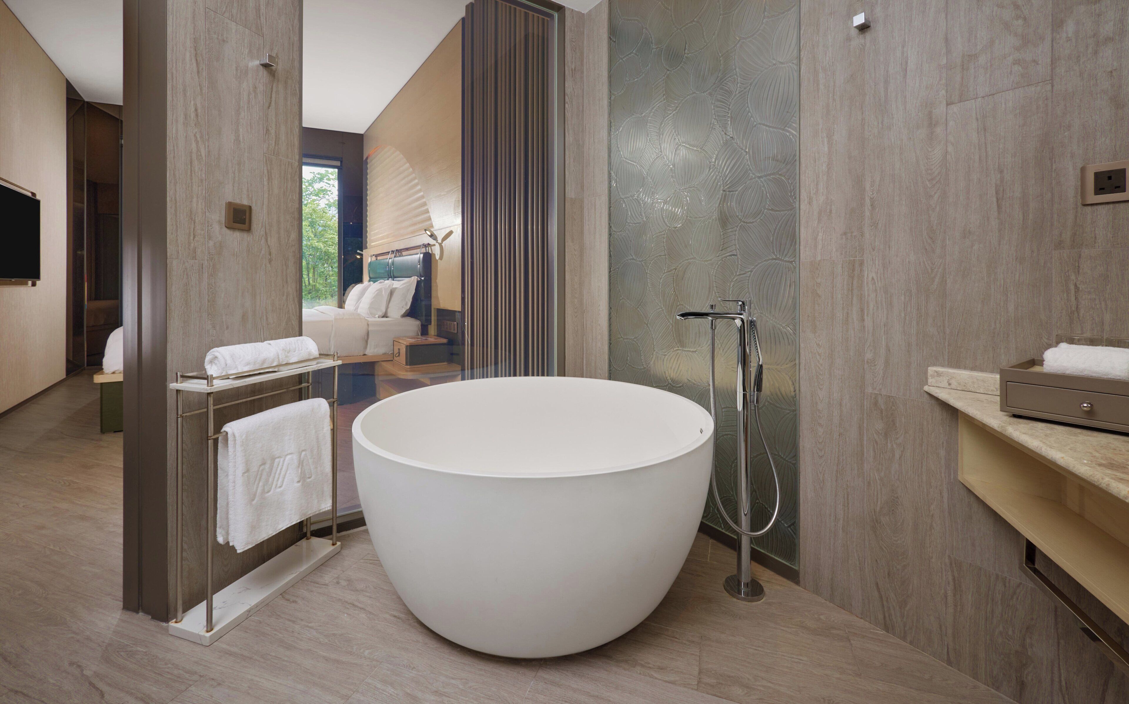A modern bathroom with a large freestanding bathtub, a walk-in shower, and a seating area with a view of the outdoors.