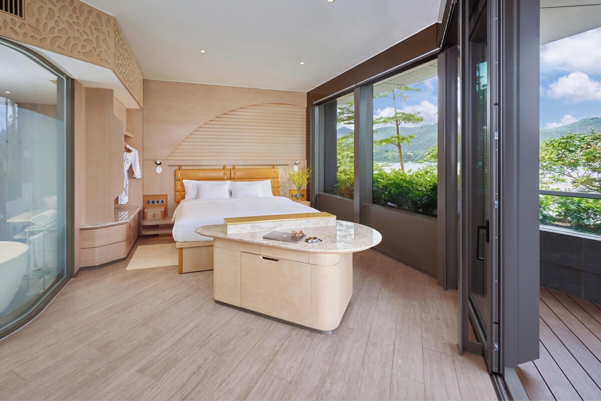 Une chambre moderne avec un grand lit, un bureau intégré et une vue sur la verdure.