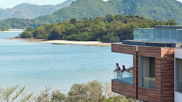 Een modern gebouw met een glazen balkon dat uitkijkt op een strand en water.