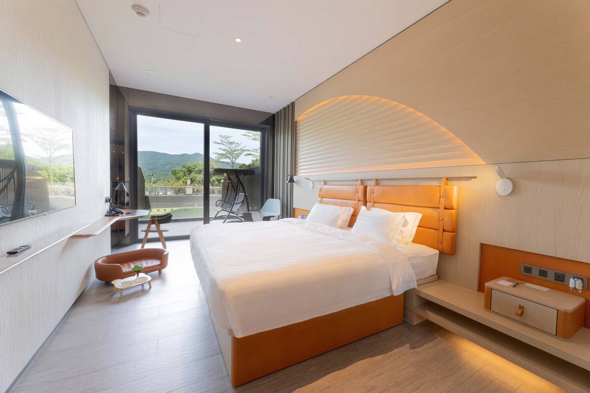 Ein modernes Hotelzimmer mit einem großen Bett, einem Schreibtisch und einem Balkon mit Bergblick.