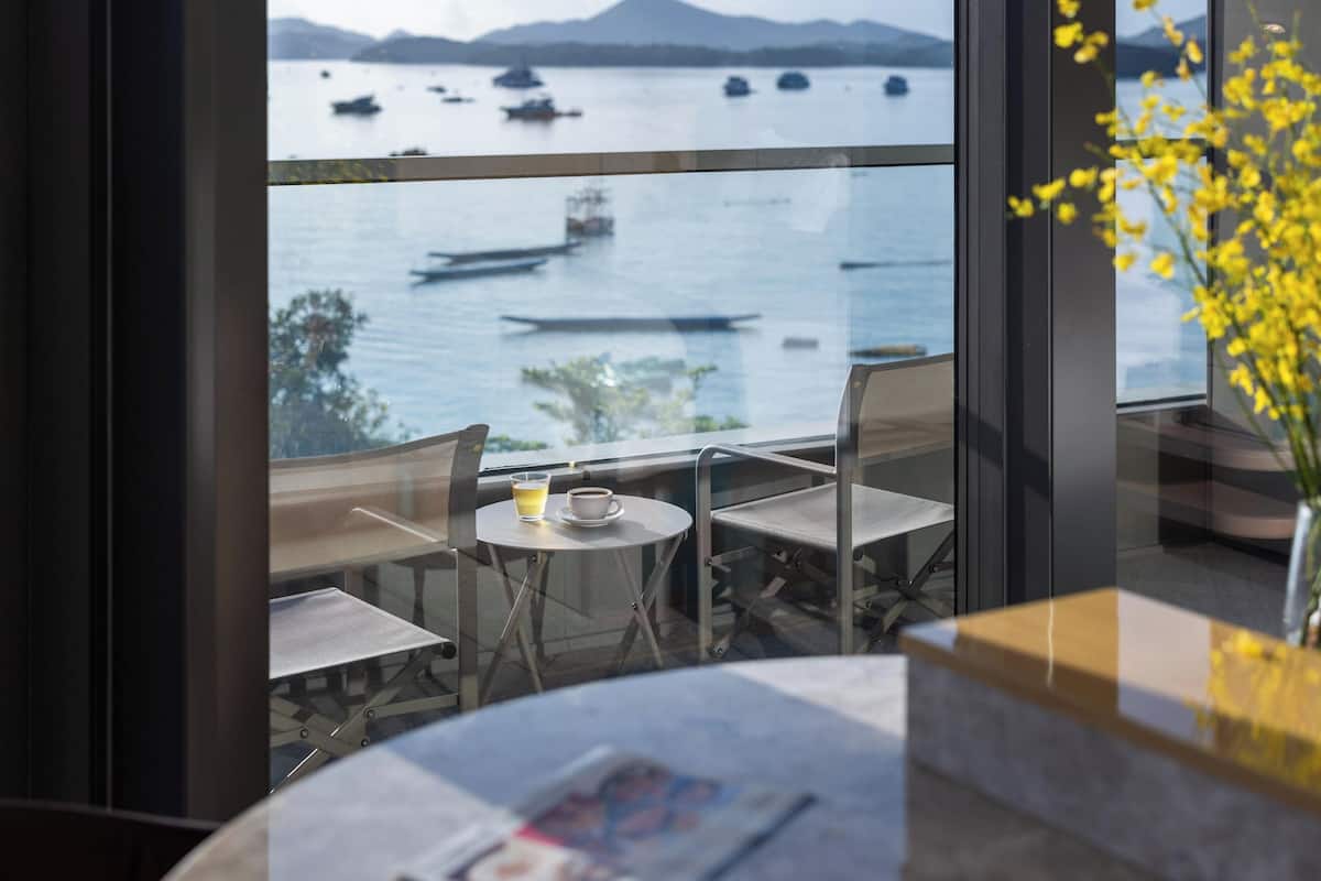 Ein Balkon mit Tisch und Stühlen, einem Getränk und Blick auf Boote auf dem Wasser.