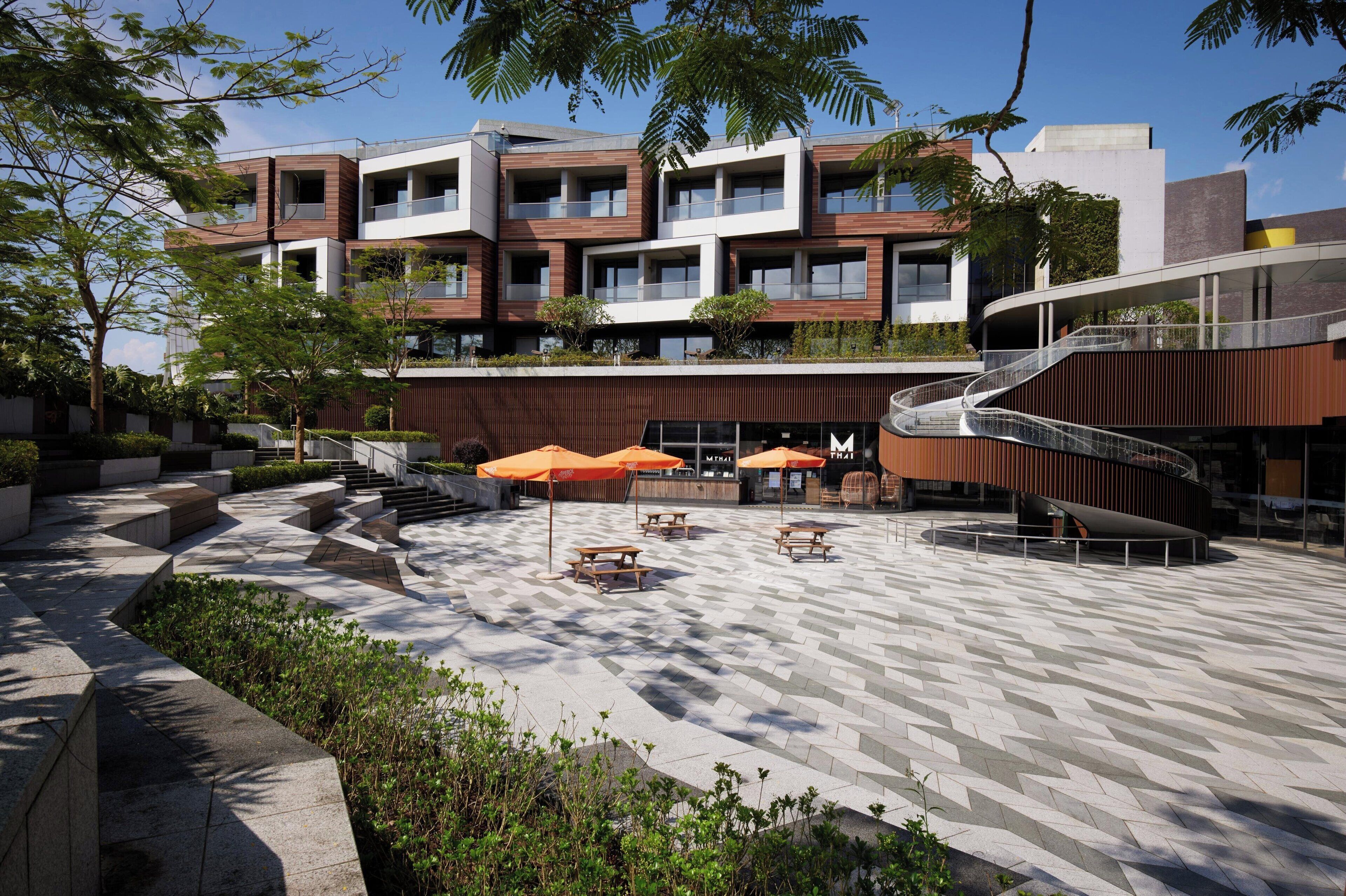 A modern building with multiple balconies, outdoor seating areas, and a central staircase.
